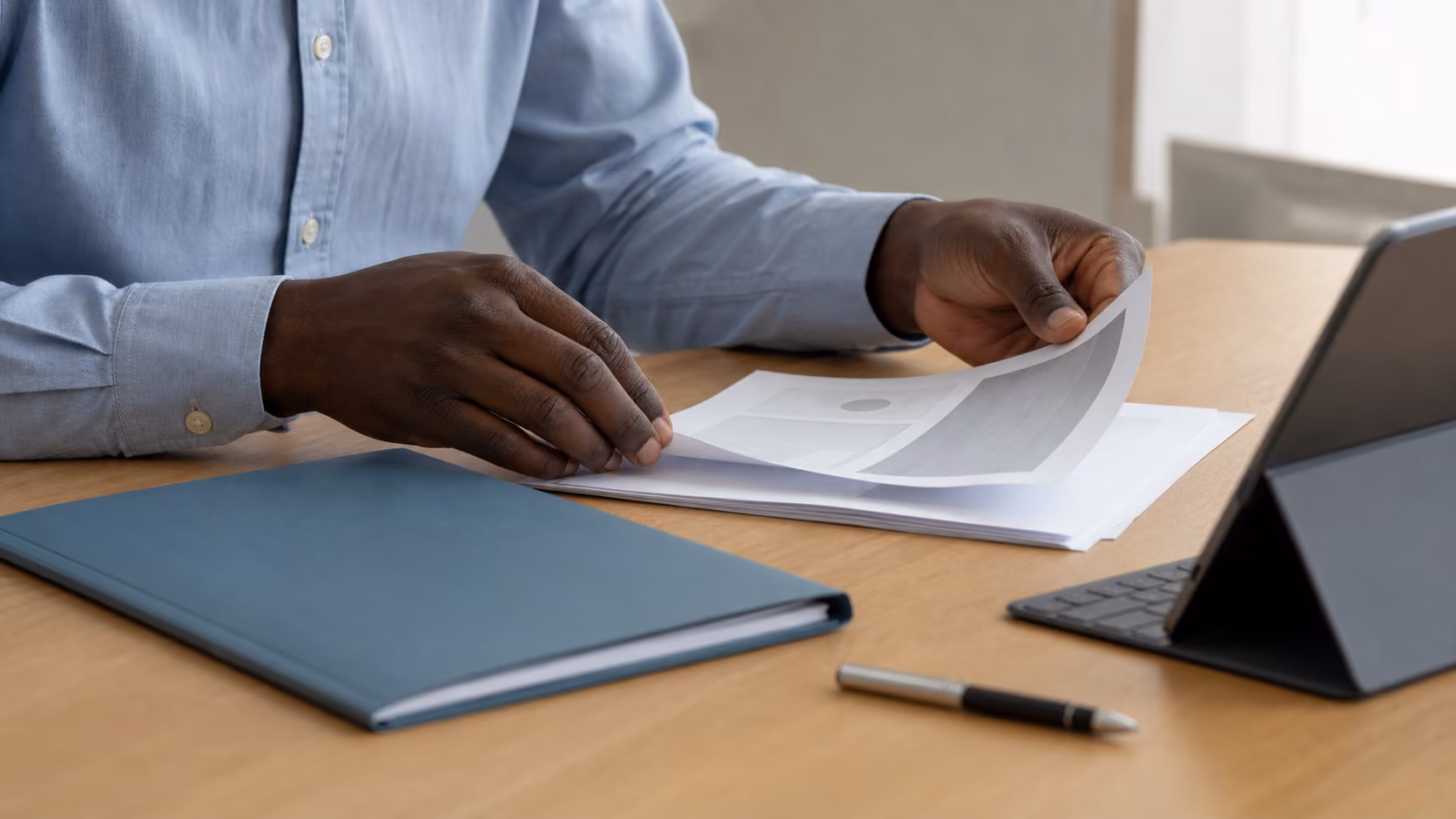 Hands reviewing printed documents beside a tablet